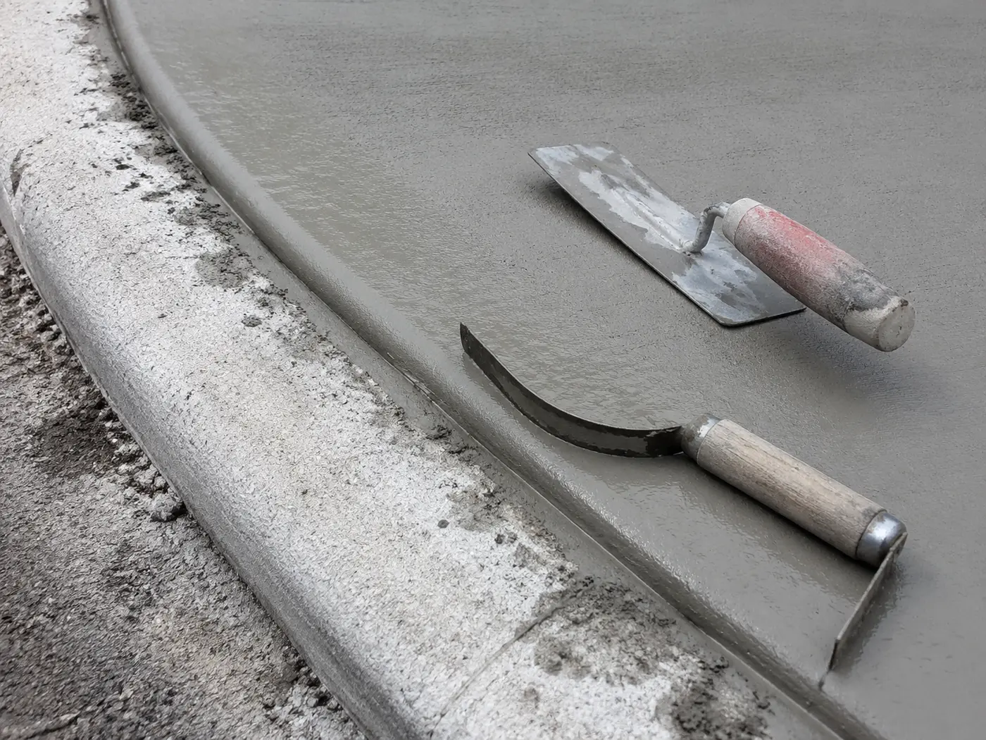 Edging tool on the wet transition where a new driveway apron meets a municipal kerb