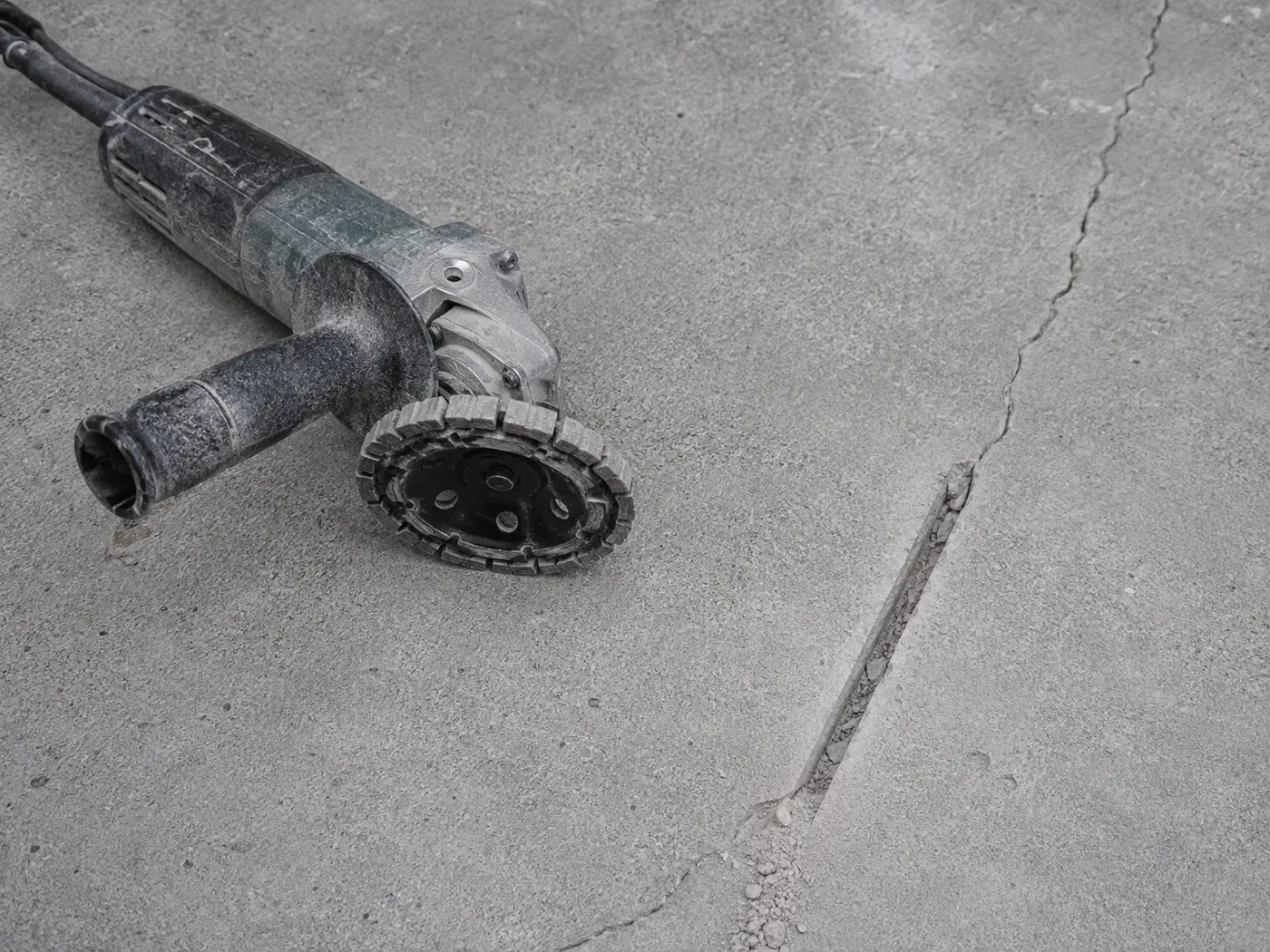 Crack-chasing wheel beside a driveway crack routed into a clean V-channel