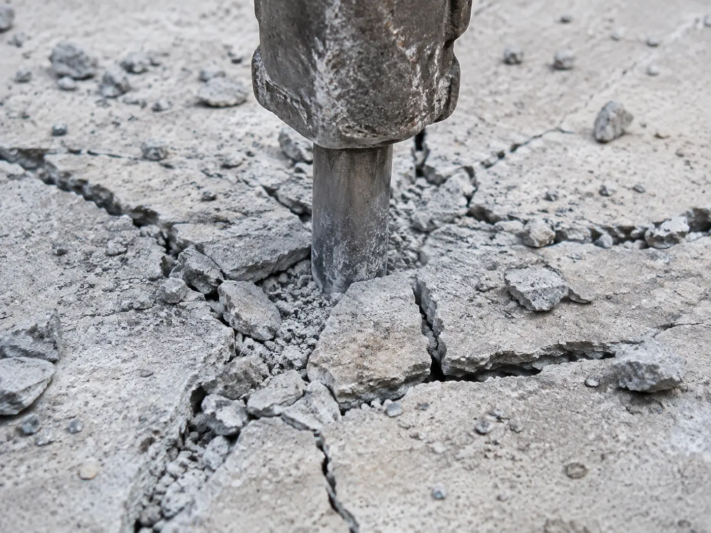 Hydraulic breaker point fracturing an old concrete driveway slab