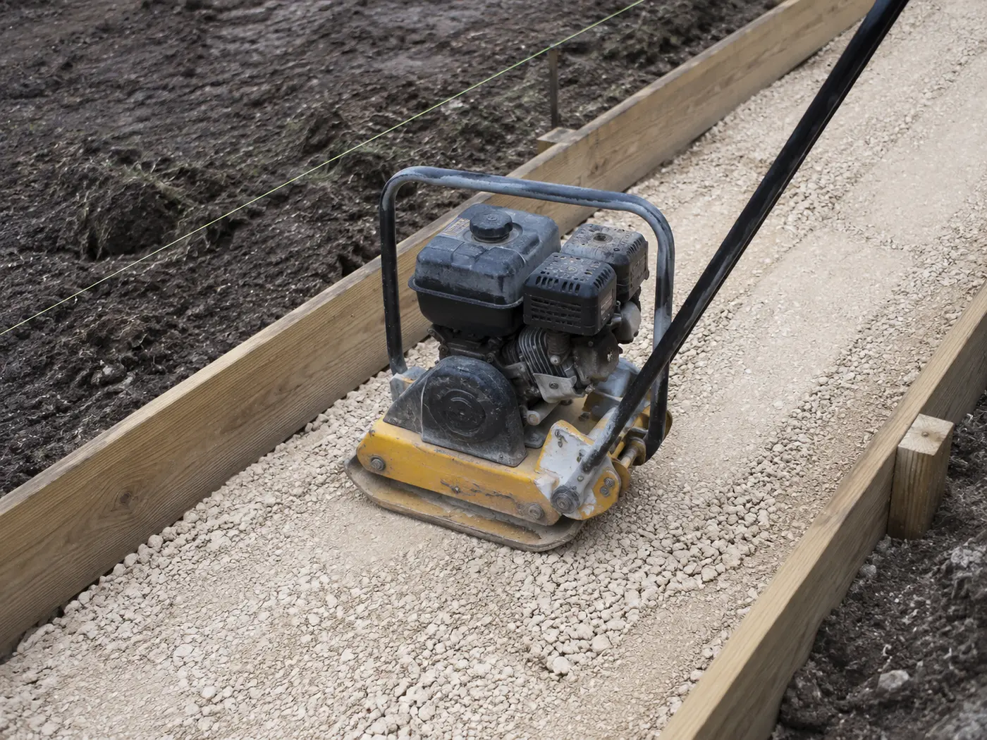 Plate compactor consolidating limerock sub-base between timber forms on a new Lakeland driveway