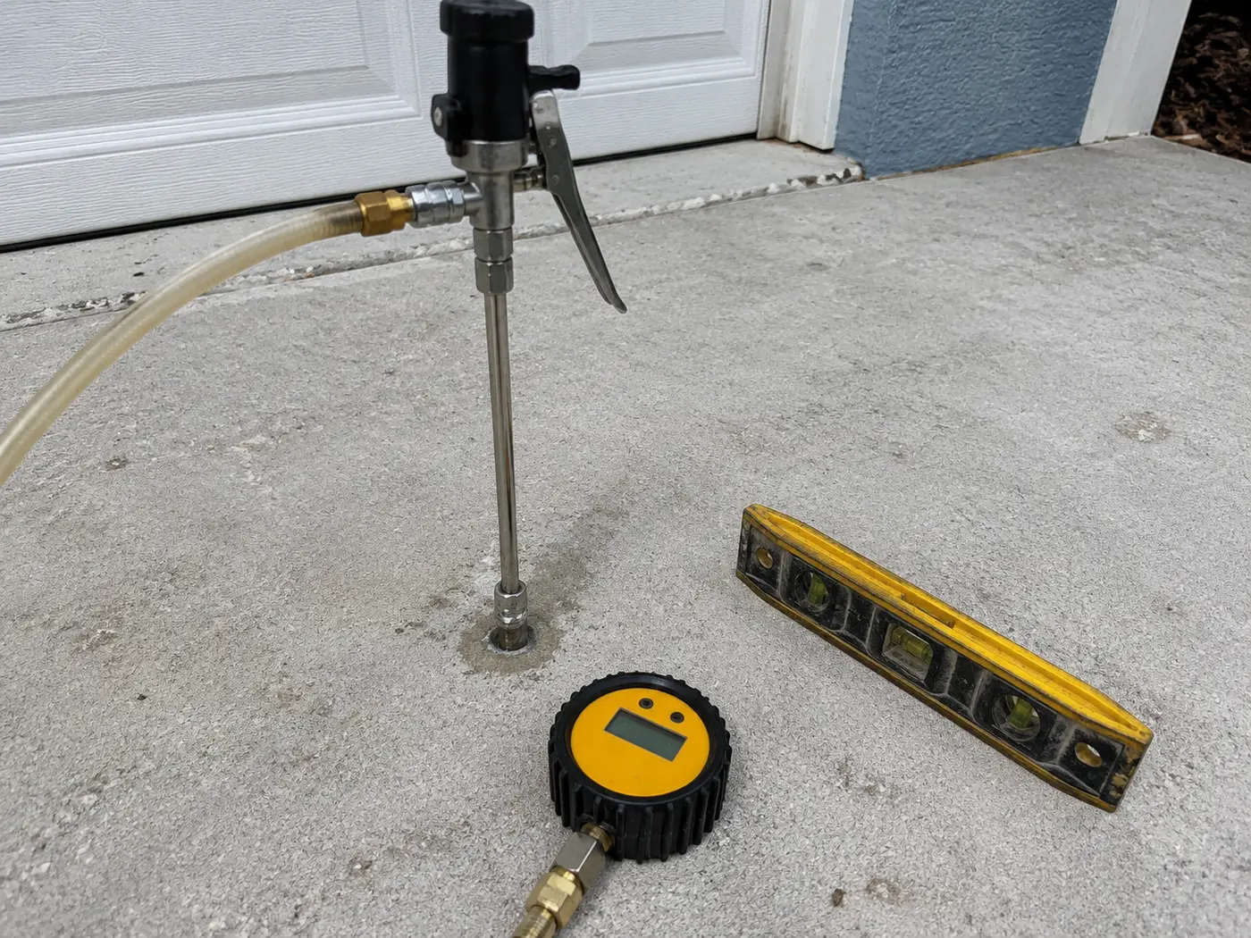 Polyurethane foam injection port drilled in a settled driveway slab with a level alongside