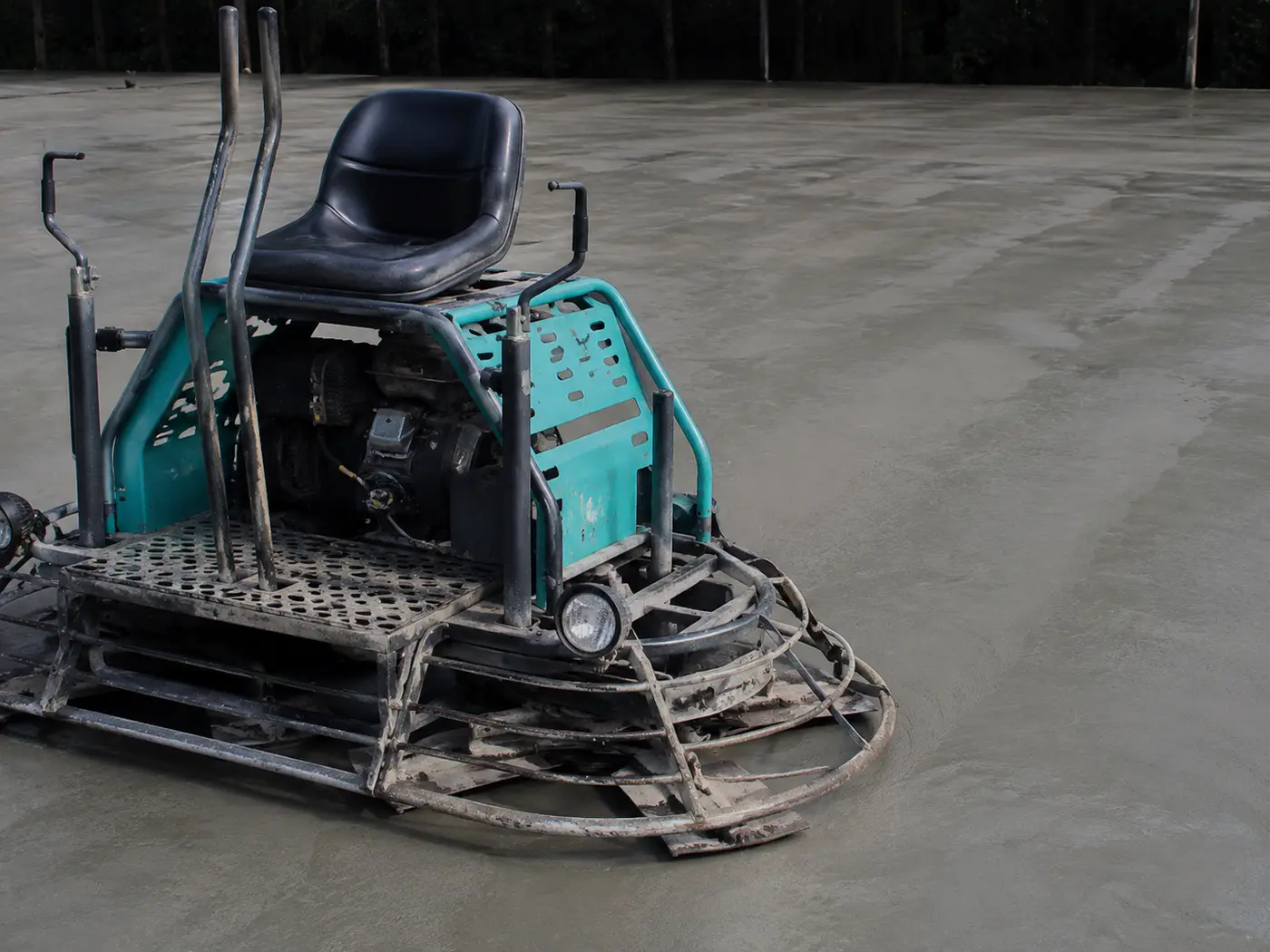 Ride-on power trowel on a large commercial slab with a hard-troweled finish trailing behind