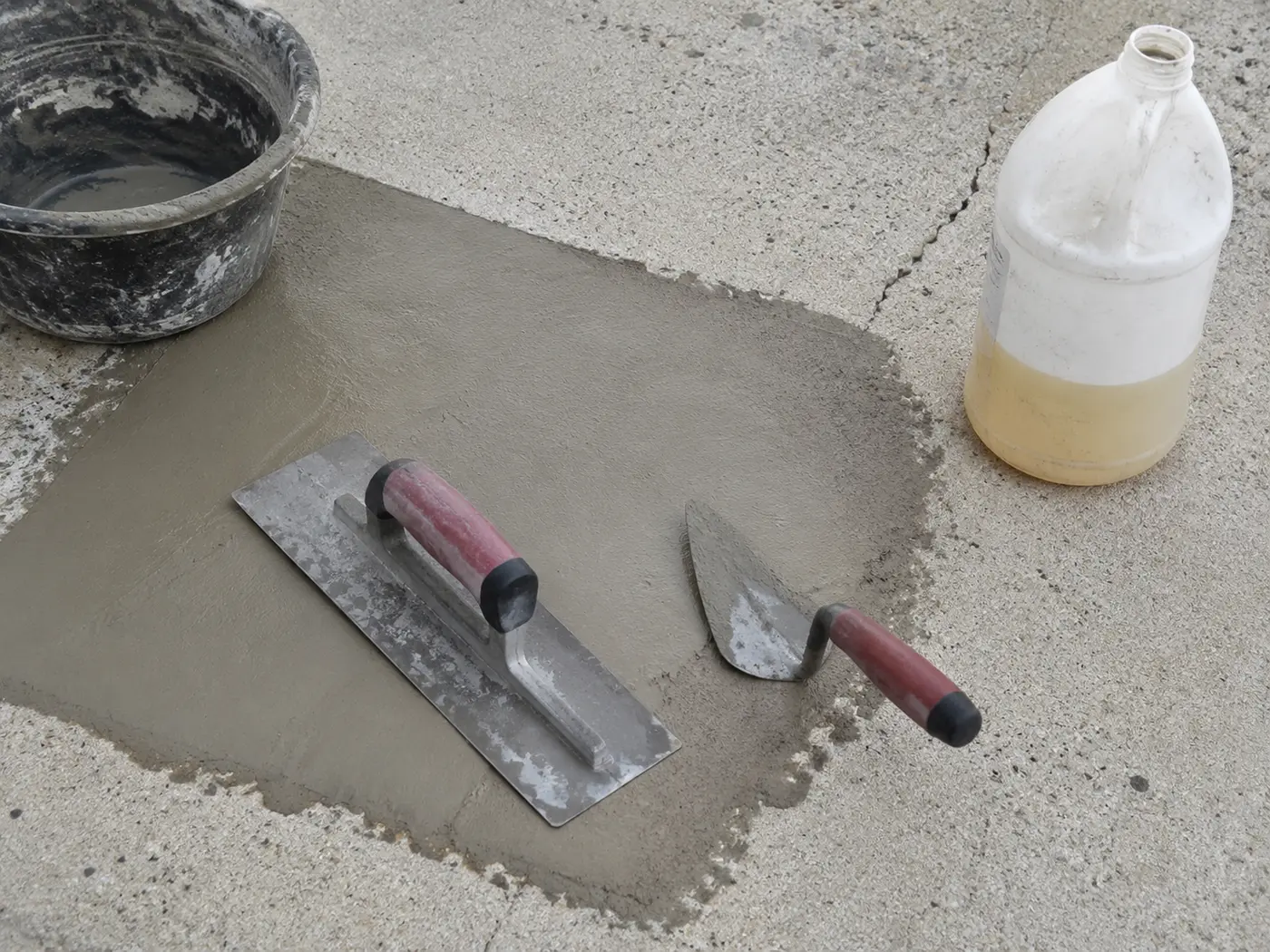 Steel trowel and margin trowel across a structural mortar patch on a concrete driveway