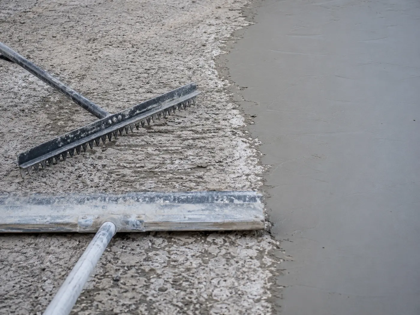Gauge rake and squeegee spreading polymer-modified overlay across a scarified slab