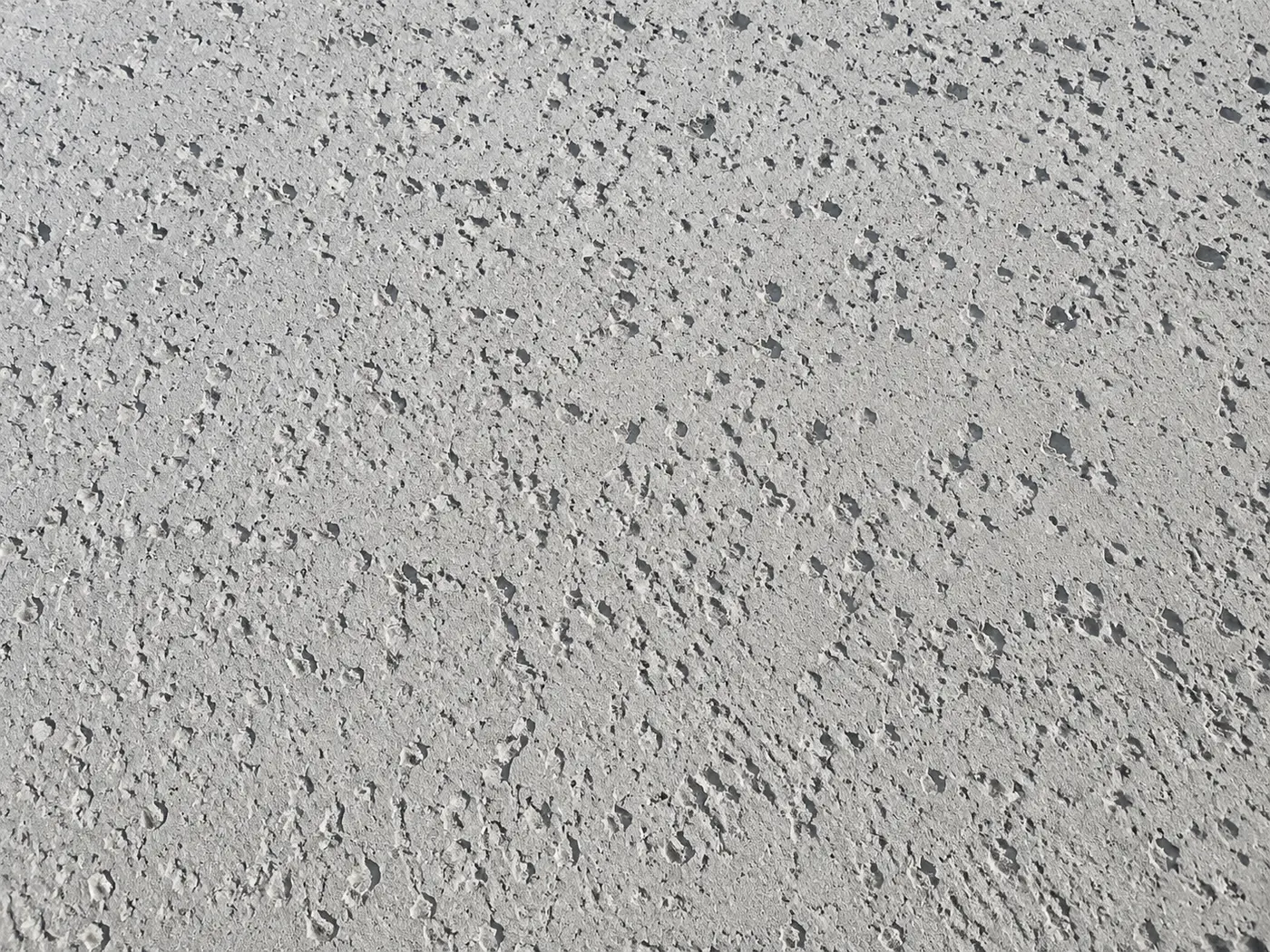 Shallow salt-finish pitting scattered across a pale concrete driveway in raking light